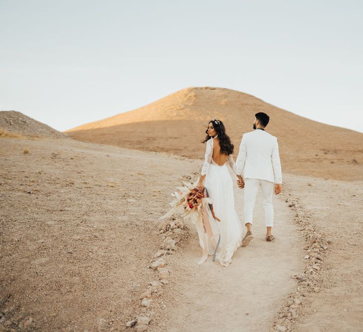 Bride in lace wedding dress and groom in white suit at desert elopement