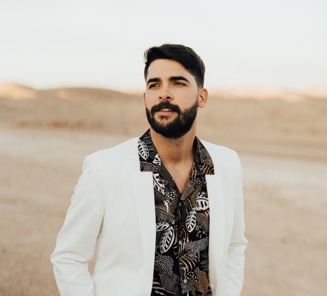 Stylish groom in white suit and patterned black shirt