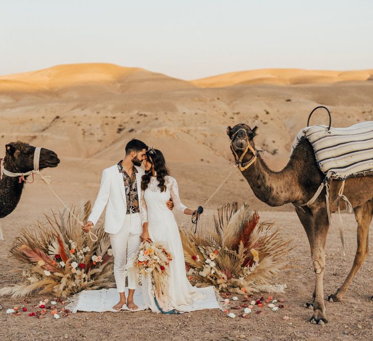 Bride and groom posing with camels at Moroccan desert wedding