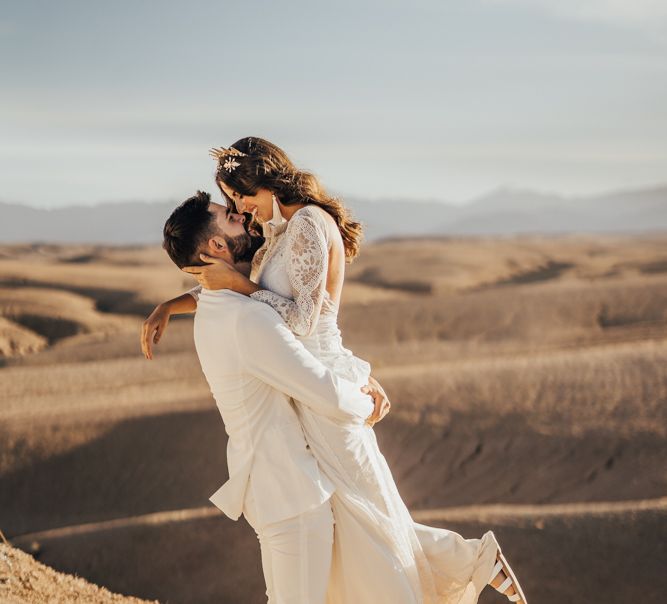 Groom in white suit picking up his boho bride