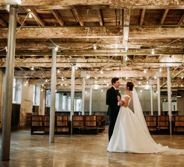 Bride and groom under festoon lighting at industrial wedding with cupcake wedding cake