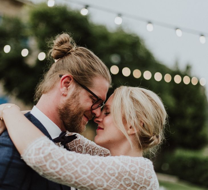 Bride in Lace Long Sleeve Rembo Styling Wedding Dress and Groom in Navy Check Blazer Embracing