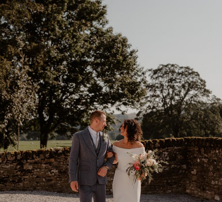 Bride in off the shoulder Suzanne Neville wedding dress and groom in grey wool suit