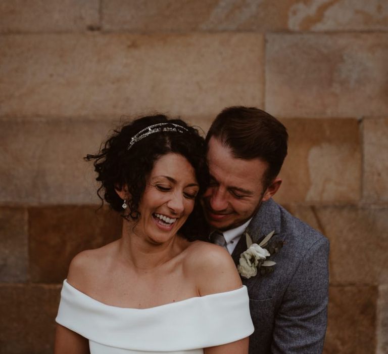 Groom in grey suit embracing his bride in off the shoulder wedding dress