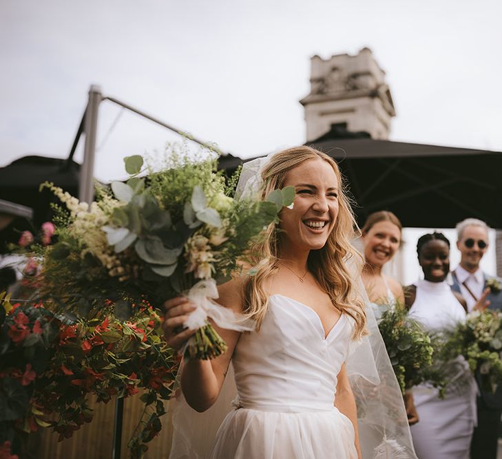 Bride in Bespoke Wedding Gown with Blush Underskirt and One Off Shoulder Strap | Fingertip Length Veil Customised with Feathers | Half Up Half Down Bridal Hair | Astrid &amp; Miyu Necklace | Homemade Bouquet of White Flowers, Ferns and Foliage | Bike Shed Motorcycle Club Wedding for ELLE Digital Editor | Nigel John Photography