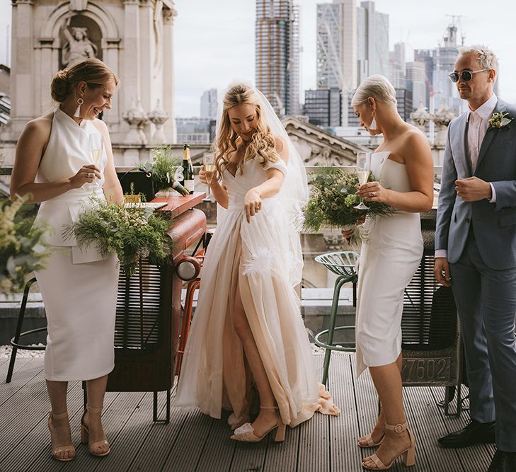 Bridal Party Champagne | Bride in Bespoke Wedding Gown with Blush Underskirt and One Off Shoulder Strap | Fingertip Length Veil Customised with Feathers | Half Up Half Down Bridal Hair | Nude Topshop Shoes with Pom Pom | Bridesmaids in Mismatched White Dresses | Bridesmen in Blue Suits | Homemade Bouquets of White Flowers, Ferns and Foliage | Bike Shed Motorcycle Club Wedding for ELLE Digital Editor | Nigel John Photography