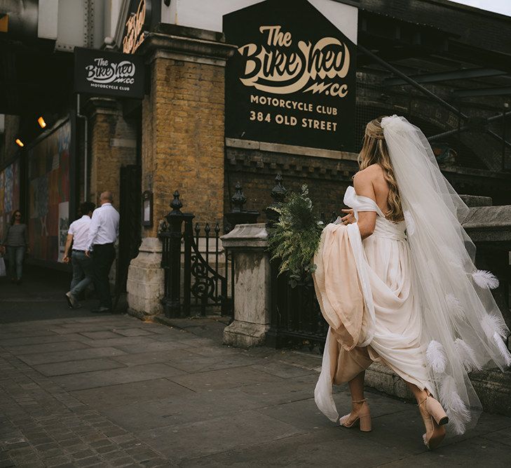 Bride Walking to Wedding Ceremony at The Bike Shed Motorcycle Club in Shoreditch | Bespoke Wedding Gown with Blush Underskirt and One Off Shoulder Strap | Fingertip Length Veil Customised with Feathers | Half Up Half Down Bridal Hair | Nude Topshop Shoes with Pom Pom | Homemade Bouquet of White Flowers, Ferns and Foliage | Bike Shed Motorcycle Club Wedding for ELLE Digital Editor | Nigel John Photography