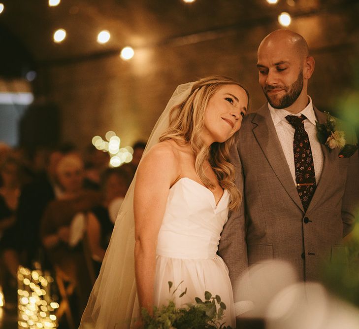 Wedding Ceremony | Bride in  Bespoke Wedding Gown with Blush Underskirt and One Off Shoulder Strap | Fingertip Length Veil Customised with Feathers | Homemade Bouquet of White Flowers, Ferns and Foliage | Groom in Grey Puppy Tooth Check Two-Piece Paul Smith Suit with Amber Tie Pin, Pocket Square and Braces | Bike Shed Motorcycle Club Wedding for ELLE Digital Editor | Nigel John Photography