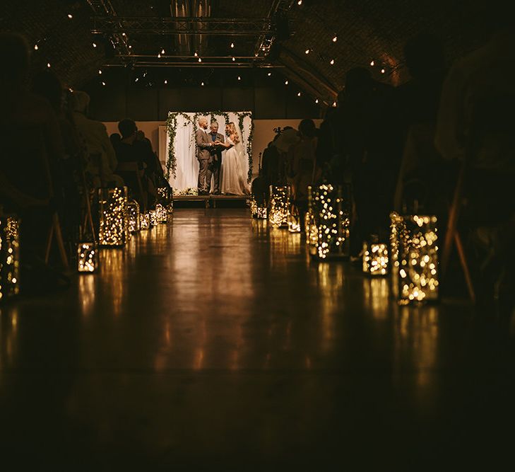 Wedding Ceremony | Bride in  Bespoke Wedding Gown with Blush Underskirt and One Off Shoulder Strap | Fingertip Length Veil Customised with Feathers | Groom in Grey Puppy Tooth Check Two-Piece Paul Smith Suit with Amber Tie Pin, Pocket Square and Braces | Lanterns Filled with Fairylights | Festoon Lights | Bike Shed Motorcycle Club Wedding for ELLE Digital Editor | Nigel John Photography