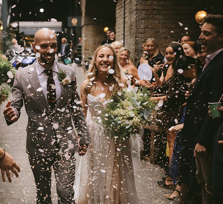 Just Married | Confetti Throw | Bride in Bespoke Wedding Gown with Blush Underskirt and One Off Shoulder Strap | Half Up Half Down Bridal Hair | Homemade Bouquet of White Flowers, Ferns and Foliage | Groom in Grey Puppy Tooth Check Two-Piece Paul Smith Suit with Amber Tie Pin, Pocket Square and Braces | Bike Shed Motorcycle Club Wedding for ELLE Digital Editor | Nigel John Photography