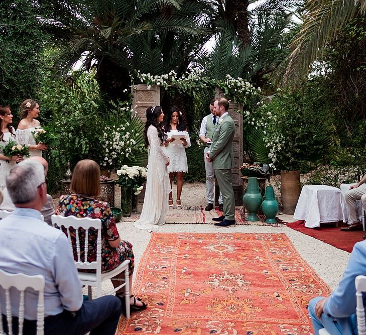 Outdoor Wedding Ceremony | Moroccan Rugs, Wooden Door Altar Wedding Decor | Bride in Rue de Seine Bridal Gown | Groom in Green Beggars Run Suit | Paradise Destination Wedding at Jnane Tamsna in Marrakech, Morocco | Nordica Photography | Matteo Castelluccia Film