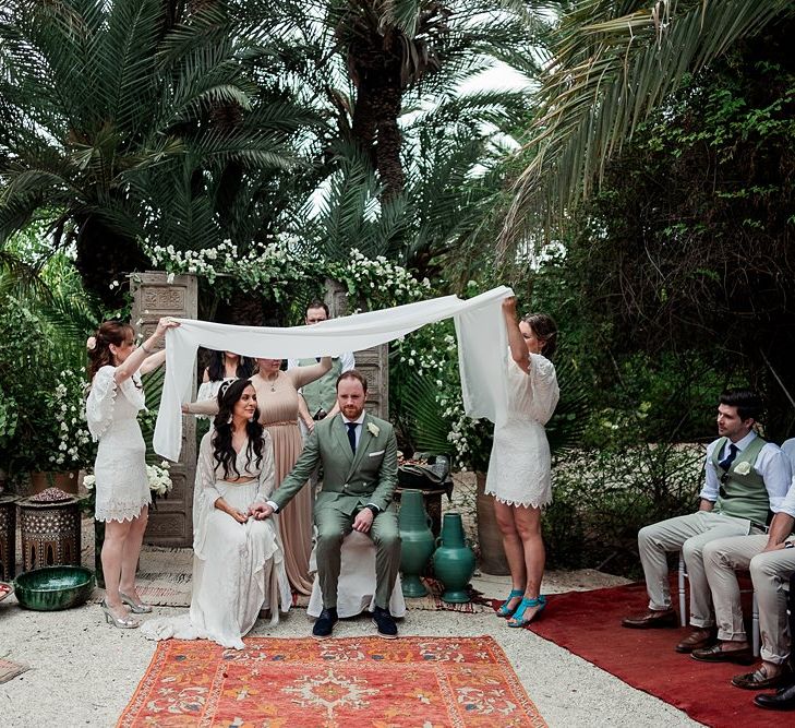 Outdoor Wedding Ceremony | Moroccan Rugs, Wooden Door Altar Wedding Decor | Bride in Rue de Seine Bridal Gown | Groom in Green Beggars Run Suit | Paradise Destination Wedding at Jnane Tamsna in Marrakech, Morocco | Nordica Photography | Matteo Castelluccia Film