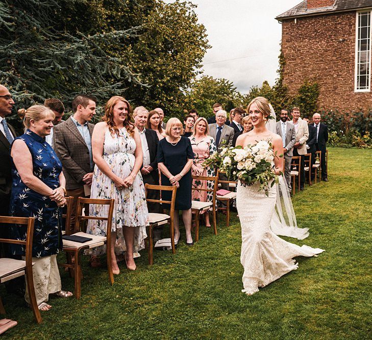 Bride walking down the aisle at outdoor Dewsall Court wedding ceremony with white bouquet