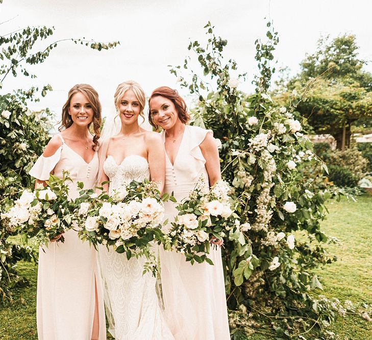 Bride with bridesmaids in cold shoulder dresses and white bouquets with floral arch decor