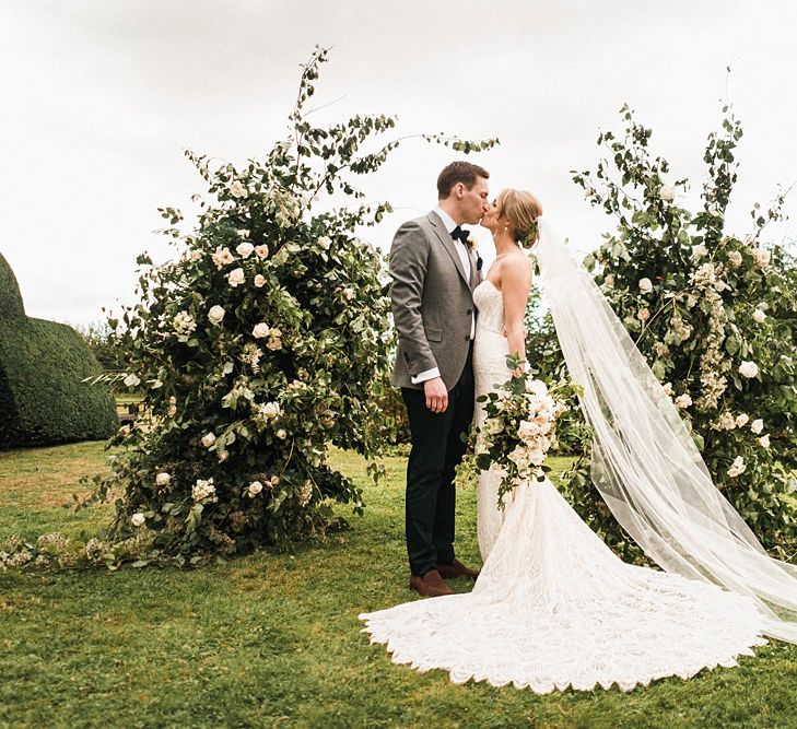 Bride in long strapless dress with groom at outdoor ceremony with floral arch