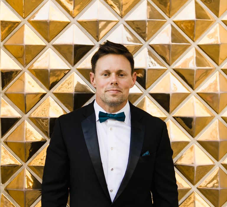 Groom in Black Tuxedo with Emerald Green Bow Tie | Las Vegas Wedding with Gold Sequin Bridesmaids Dresses and Silk Flowers | Chris Barber Photography