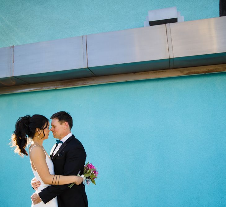 Bride in Silk BHLDN Dress with Spaghetti Straps and V-Back | Groom in Black Tuxedo with Emerald Green Bow Tie | Fuschia Sweet Pea Spray Silk Flowers Bouquet | Bridal Ponytail | First Look Photo | Las Vegas Wedding with Gold Sequin Bridesmaids Dresses and Silk Flowers | Chris Barber Photography