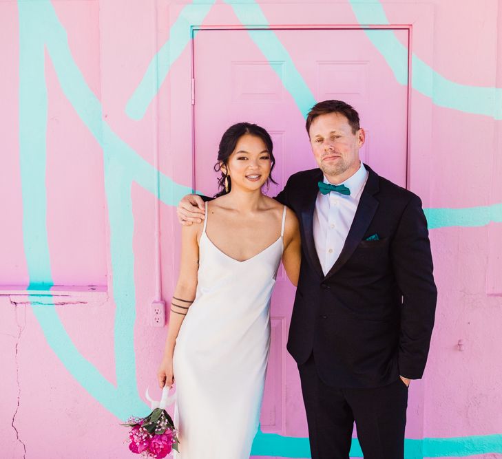 Bride in Silk BHLDN Dress with Spaghetti Straps and V-Back | Groom in Black Tuxedo with Emerald Green Bow Tie | Fuschia Sweet Pea Spray Silk Flowers Bouquet | Bridal Ponytail | First Look Photo | Las Vegas Wedding with Gold Sequin Bridesmaids Dresses and Silk Flowers | Chris Barber Photography