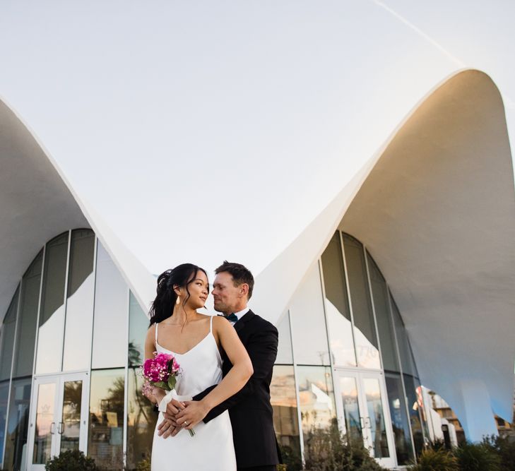 Bride in Silk BHLDN Dress with Spaghetti Straps and V-Back | Groom in Black Tuxedo with Emerald Green Bow Tie | Fuschia Sweet Pea Spray Silk Flowers Bouquet | Bridal Ponytail | Las Vegas Wedding with Gold Sequin Bridesmaids Dresses and Silk Flowers | Chris Barber Photography