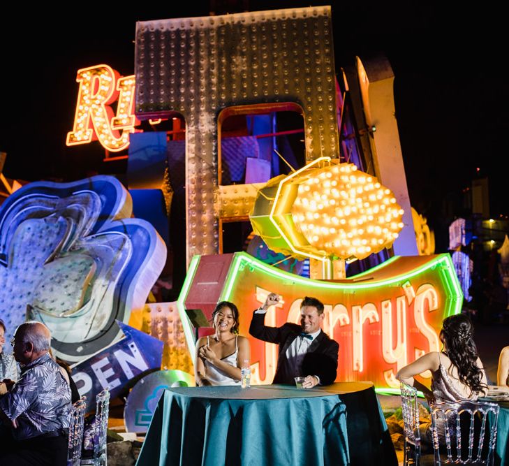 Bride in Silk BHLDN Dress with Spaghetti Straps and V-Back | Groom in Black Tuxedo with Emerald Green Bow Tie | Bridal Ponytail | The Neon Museum | Las Vegas Wedding with Gold Sequin Bridesmaids Dresses and Silk Flowers | Chris Barber Photography