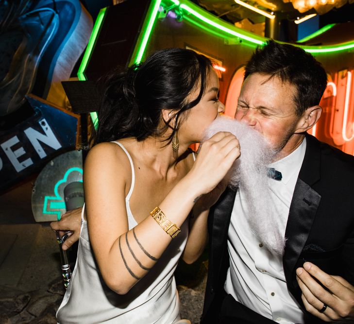 Bride in Silk BHLDN Dress with Spaghetti Straps and V-Back | Groom in Black Tuxedo with Emerald Green Bow Tie | Bridal Ponytail | Cotton Candy Machine | The Neon Museum | Las Vegas Wedding with Gold Sequin Bridesmaids Dresses and Silk Flowers | Chris Barber Photography