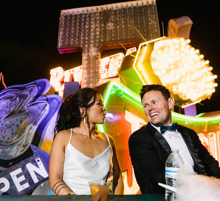 Bride in Silk BHLDN Dress with Spaghetti Straps and V-Back | Groom in Black Tuxedo with Emerald Green Bow Tie | Bridal Ponytail | The Neon Museum | Las Vegas Wedding with Gold Sequin Bridesmaids Dresses and Silk Flowers | Chris Barber Photography