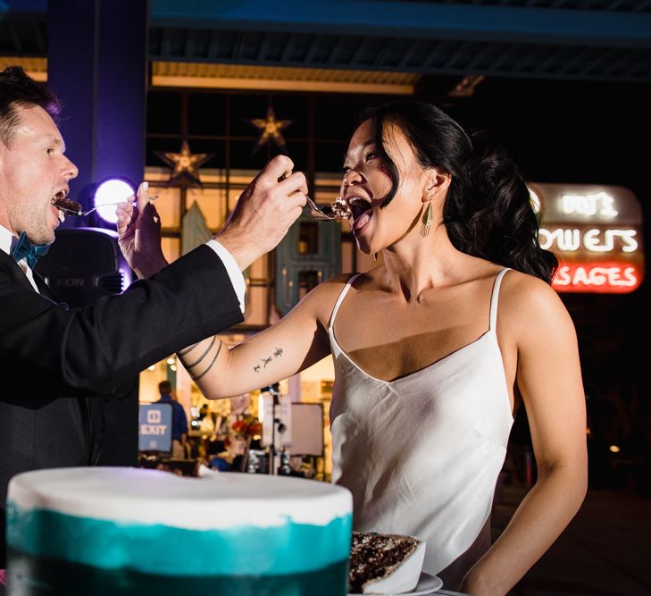 Wedding Cake with White, Green and Gold Icing | Bride in Silk BHLDN Dress with Spaghetti Straps and V-Back | Groom in Black Tuxedo with Emerald Green Bow Tie | Bridal Ponytail | The Neon Museum | Las Vegas Wedding with Gold Sequin Bridesmaids Dresses and Silk Flowers | Chris Barber Photography