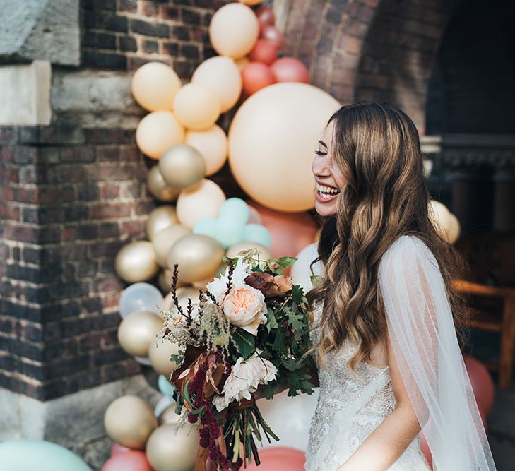 Bride wearing embellished custom made dress with peach wedding flowers and balloon installation