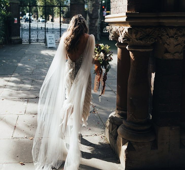 Back of brides dress with long detachable train and peach wedding flowers mixed with dried foliage and tied with vintage trim