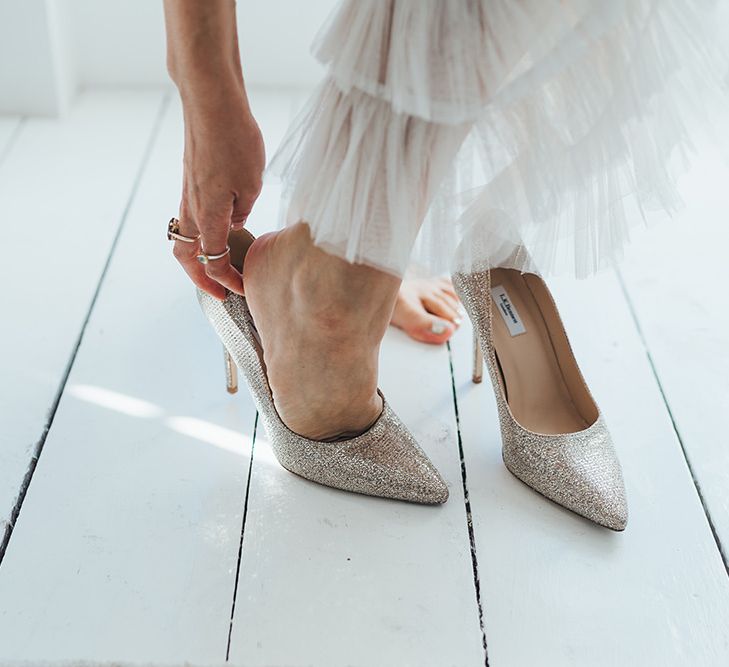 Bride putting on gold glitter stiletto wedding shoes at a relaxed wedding with balloon installation