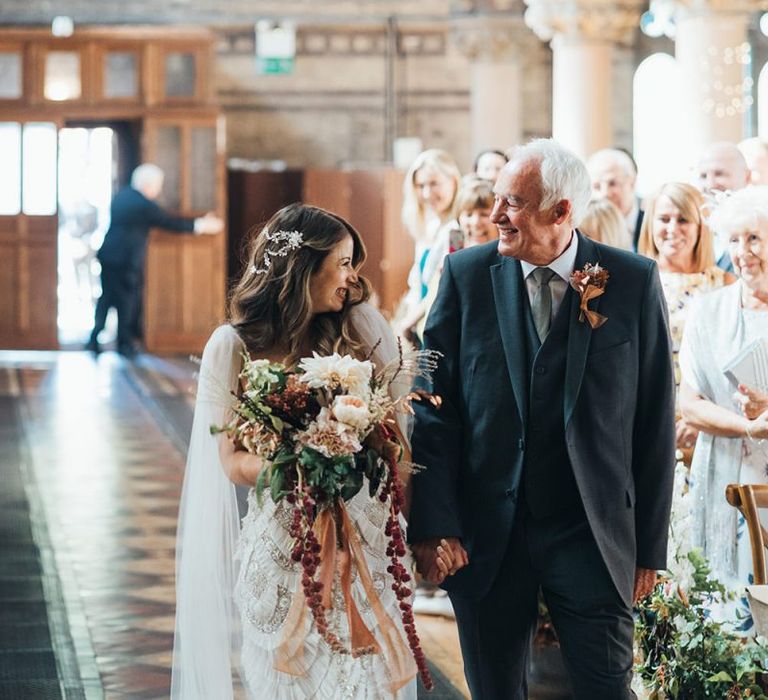 Bride walking down the aisle wearing custom made dress, embellished hair accessory and watteau train