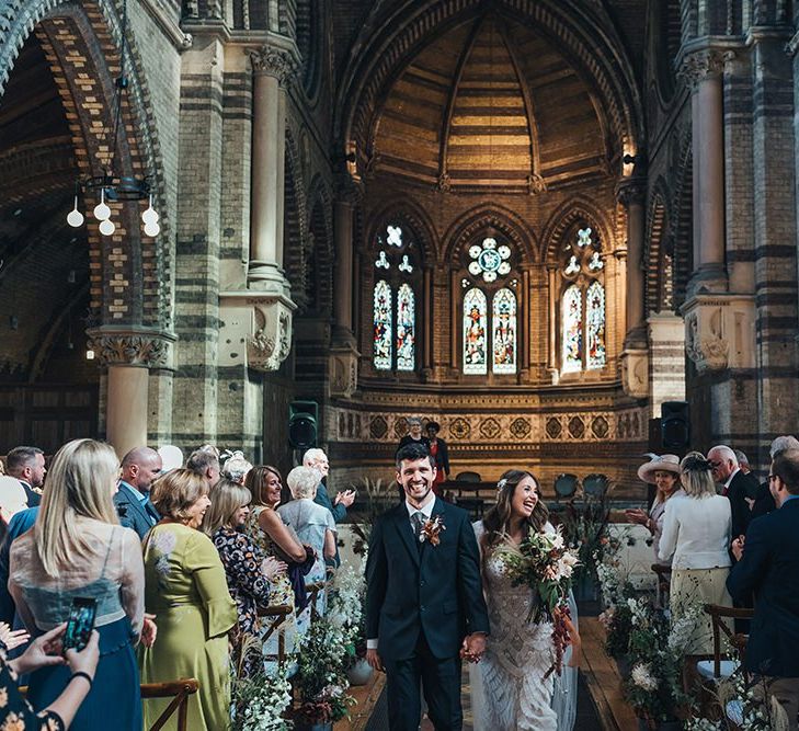 Bride and groom tie the knot at church ceremony wearing custom made embellished dress and peach wedding flowers mixed with dried foliage