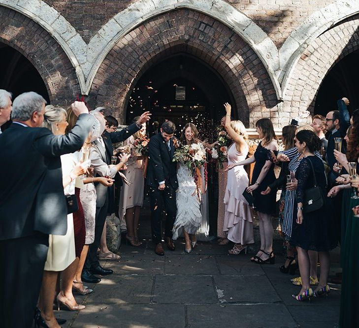 Church confetti moment with bride wearing embellished dress and peach wedding flowers tied with vintage trim