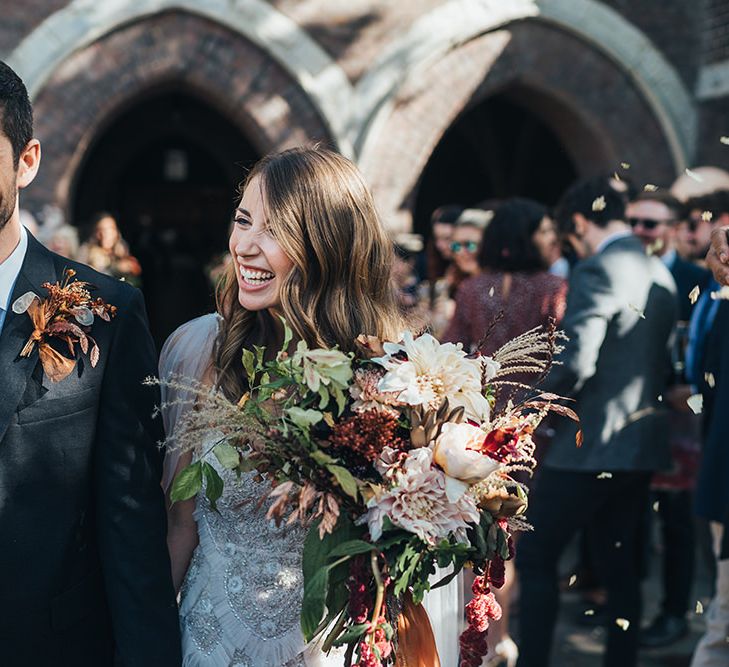 Groom wearing dried floral buttonhole arrangement and bride holding peach wedding flowers tied with vintage trim