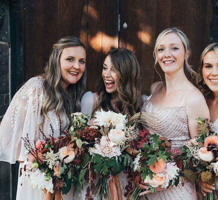 Bride with her bridesmaids wearing embellished dress and peach wedding flowers mixed with dried foliage and tied with vintage trim