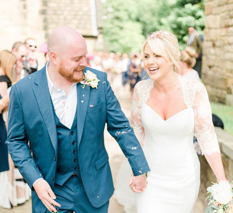 Stylish Bride in Suzanne Neville Wedding Dress and Lace Bolero and Groom in Navy Hugo Boss Suit Showered in Confetti