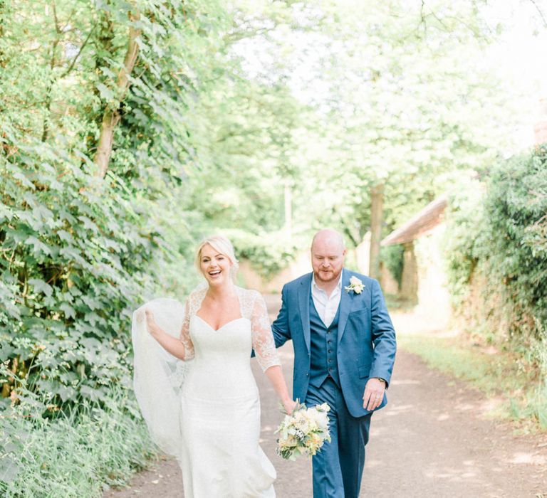 Bride in Suzanne Neville Wedding Dress and Lace Bolero and Groom in Navy Hugo Boss Suit  Walking Down a Country Lane