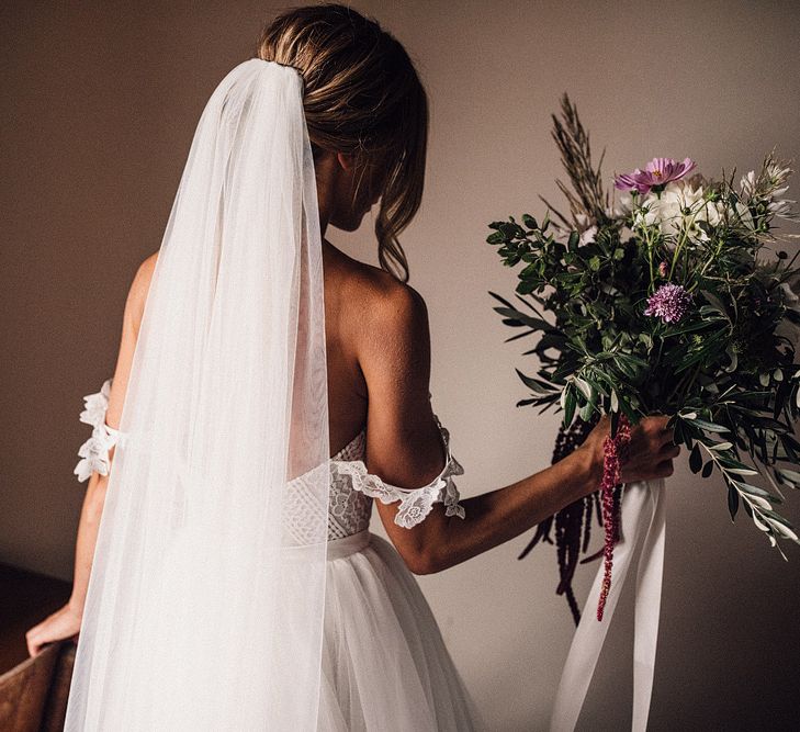 Bride in Structured Bustier Rue de Seine Fox Gown with Floral Appliqué Detail and Off The Shoulder Straps | Pronovias Chiffon Overskirt | Pink, Purple and White Wildflower Bouquet with White Trailing Ribbon | Rue de Seine Wedding Dress with Pronovias Overskirt, Personalised Place Setting Illustrations and Sweetheart Table | Samuel Docker Photography