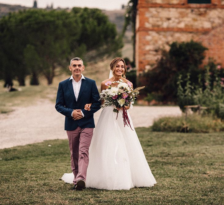 Bride in Structured Bustier Rue de Seine Fox Gown with Floral Appliqué Detail and Off The Shoulder Straps | Pronovias Chiffon Overskirt | Pink, Purple and White Wildflower Bouquet with White Trailing Ribbon | Outdoor Wedding Ceremony at Il Rigo Agriturismo, Tuscany | Rue de Seine Wedding Dress with Pronovias Overskirt, Personalised Place Setting Illustrations and Sweetheart Table | Samuel Docker Photography