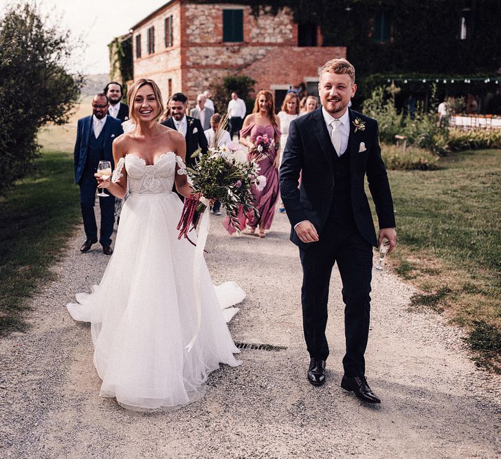 Bride in Structured Bustier Rue de Seine Fox Gown with Floral Appliqué Detail and Off The Shoulder Straps | Pronovias Chiffon Overskirt | Pink, Purple and White Wildflower Bouquet with White Trailing Ribbon | Groom in Three-Piece Hawes &amp; Curtis Suit with Ivory Tie and Pocket Square | Rue de Seine Wedding Dress with Pronovias Overskirt, Personalised Place Setting Illustrations and Sweetheart Table | Samuel Docker Photography