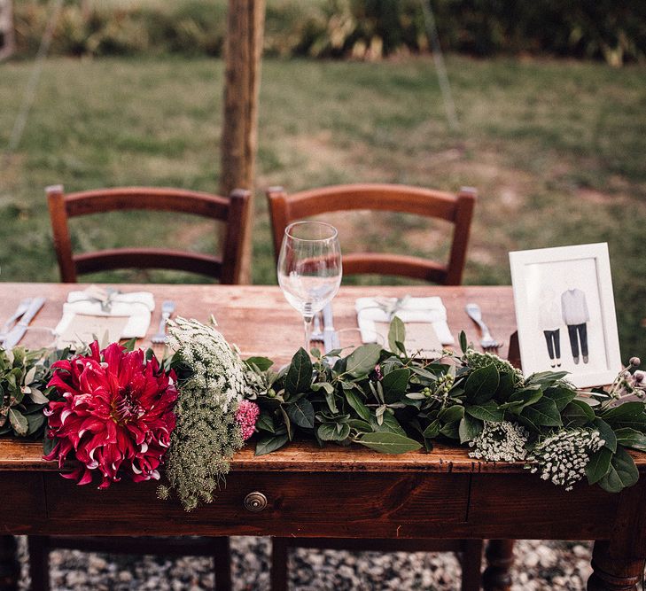 Rustic Wooden Sweetheart Table | Table Runner with Pink Flowers and Foliage | Illustrated Place Setting in White Frame | Rue de Seine Wedding Dress with Pronovias Overskirt, Personalised Place Setting Illustrations and Sweetheart Table | Samuel Docker Photography