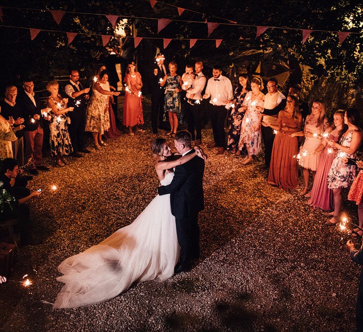 Bride in Structured Bustier Rue de Seine Fox Gown with Floral Appliqué Detail and Off The Shoulder Straps | Pronovias Chiffon Overskirt | Groom in Three-Piece Hawes &amp; Curtis Suit with Ivory Tie and Pocket Square | Sparklers | Outdoor Wedding Reception at Il Rigo Agriturismo, Tuscany | Rue de Seine Wedding Dress with Pronovias Overskirt, Personalised Place Setting Illustrations and Sweetheart Table | Samuel Docker Photography