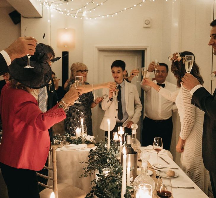 Bride and groom toast with their guests at intimate reception with foliage table decor and taper candles