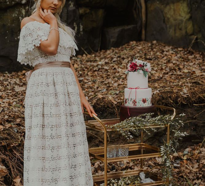 Bride Standing Next to a Gold Drinks Trolley with Three Tier Wedding Cake on Top