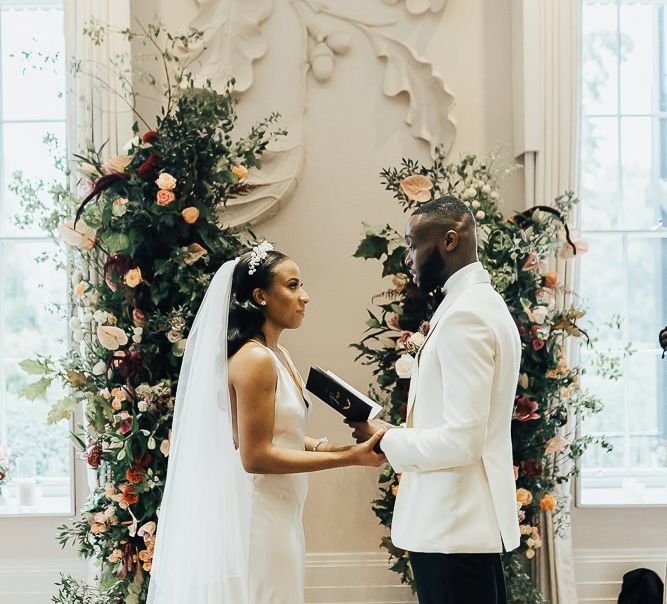 Groom in white tuxedo jacket reading his vows