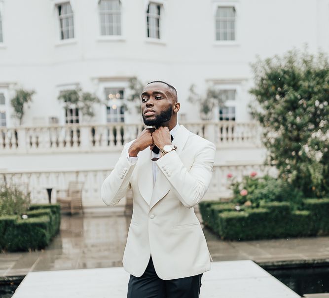 Stylish groom in white tuxedo jacket and bow tie for Coworth Park wedding