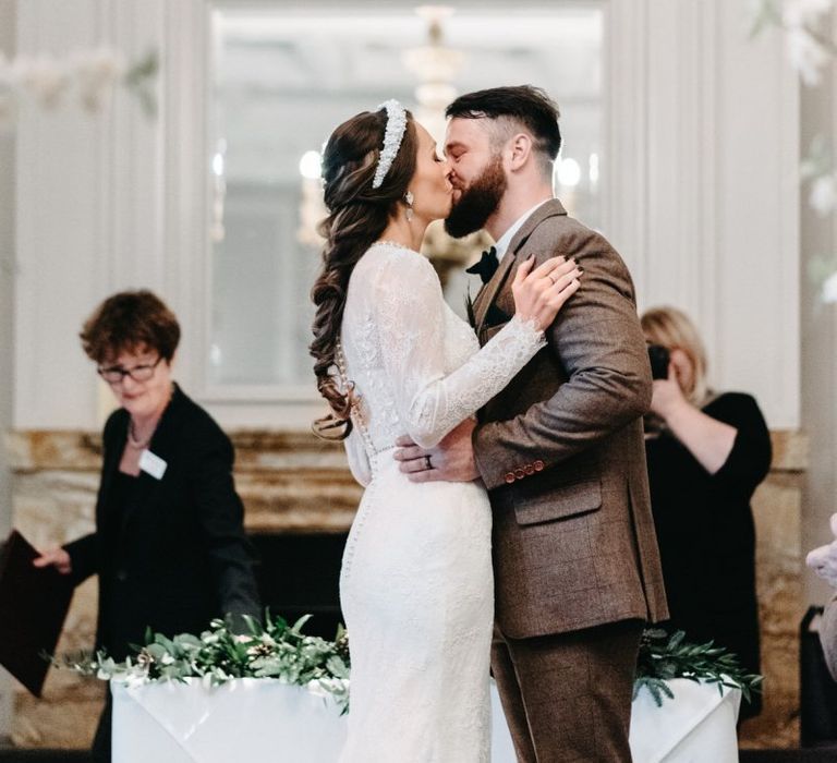 Bride and groom kiss wearing tweed wedding suit and bridal braid