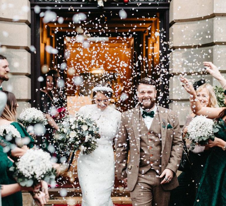 Confetti shot with groom wearing tweed wedding suit and bride with embellished headband and lace detailed dress