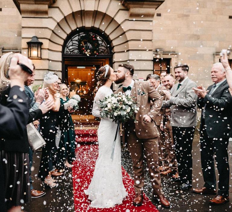 Confetti shot with groom wearing tweed wedding suit and bride with embellished headband and lace detailed dress