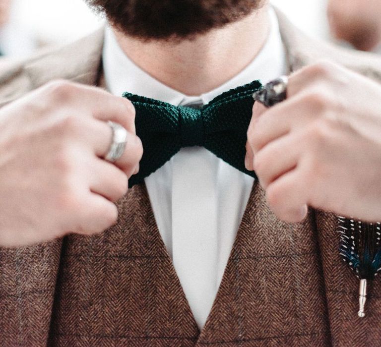 Groom wearing tweed wedding suit and green bow tie at winter celebration